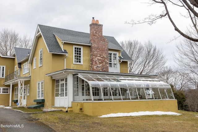 back of house with stucco siding, roof with shingles, and a chimney