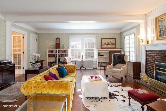 living area featuring a brick fireplace, wallpapered walls, crown molding, and wood finished floors