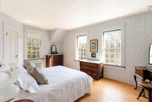 bedroom with wallpapered walls, light wood-style flooring, radiator, and baseboards