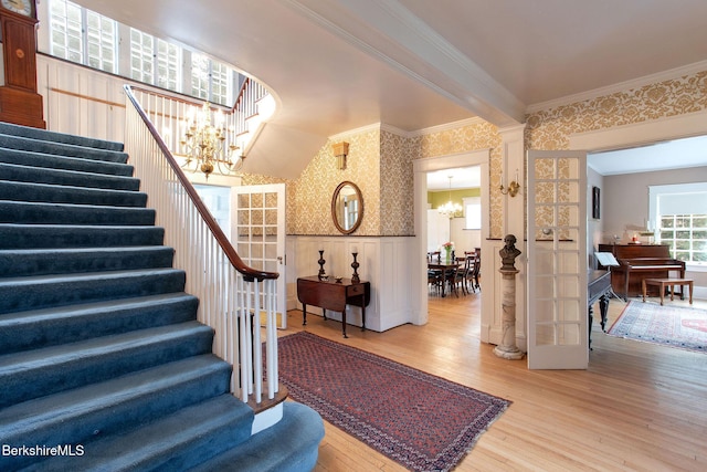 staircase featuring wallpapered walls, wood finished floors, an inviting chandelier, crown molding, and wainscoting