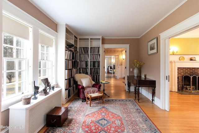 sitting room featuring light wood-style flooring, a fireplace, crown molding, and baseboards