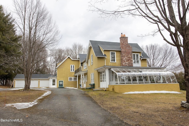 exterior space featuring a balcony, a sunroom, stucco siding, a chimney, and a detached garage