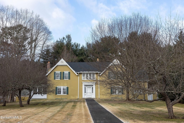 traditional-style house with stucco siding, driveway, a chimney, and a front lawn