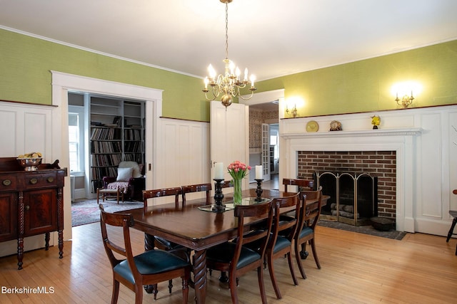 dining room with a decorative wall, light wood-style floors, crown molding, a fireplace, and wainscoting