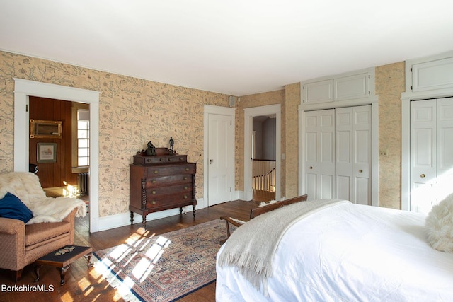 bedroom with two closets, baseboards, dark wood-type flooring, and wallpapered walls