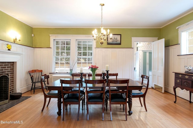 dining room featuring a decorative wall, a fireplace, light wood finished floors, and ornamental molding