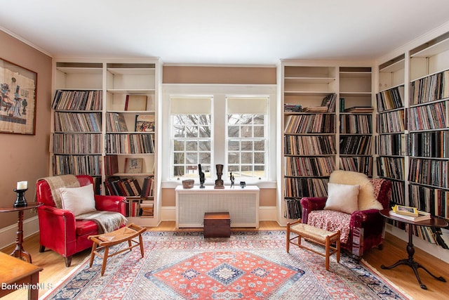 sitting room with wall of books, radiator heating unit, wood finished floors, and baseboards