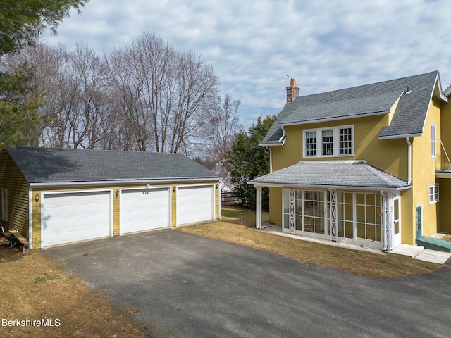 view of front of property featuring roof with shingles, a sunroom, stucco siding, a chimney, and a garage