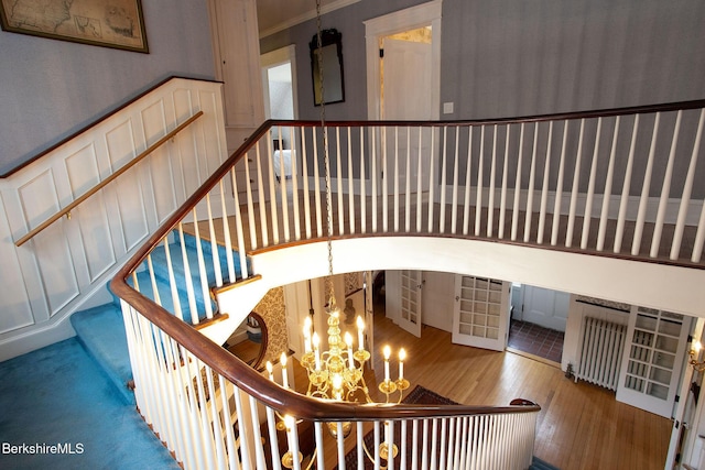 stairway with a wainscoted wall, ornamental molding, an inviting chandelier, wood finished floors, and a decorative wall