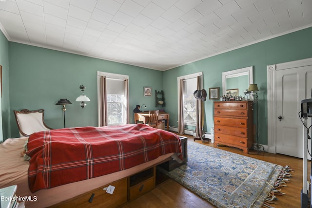 bedroom with a baseboard radiator, wood finished floors, and crown molding