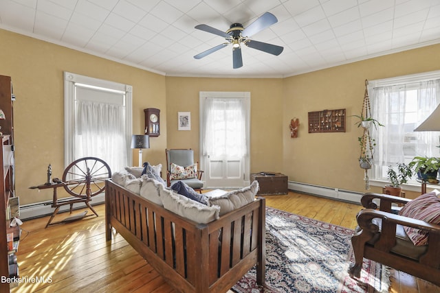 living area with ornamental molding, a baseboard heating unit, and hardwood / wood-style flooring