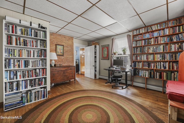 living area featuring a baseboard heating unit, wood finished floors, and a drop ceiling