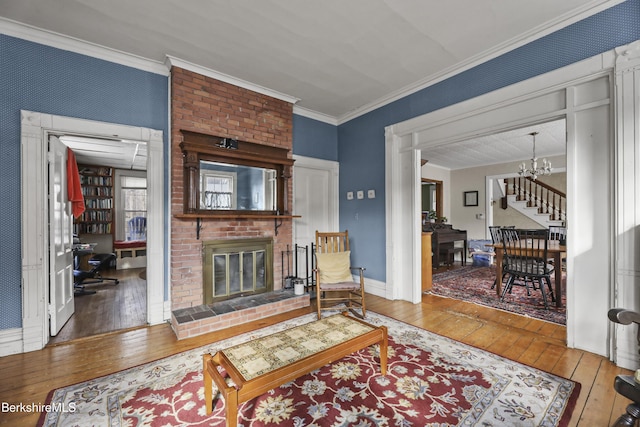 living area with a brick fireplace, wood-type flooring, an inviting chandelier, and crown molding