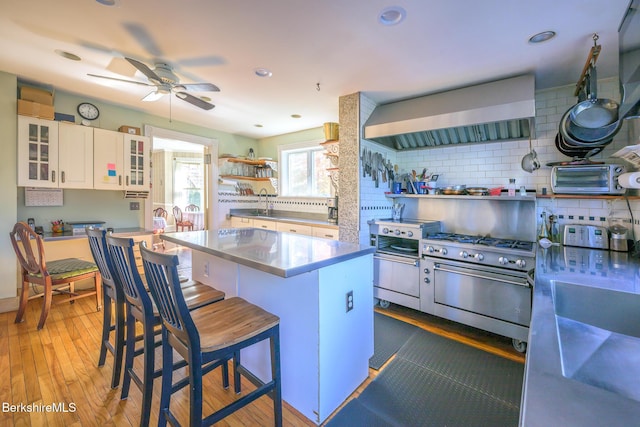 kitchen with decorative backsplash, a kitchen bar, wall chimney exhaust hood, a kitchen island, and white cabinetry