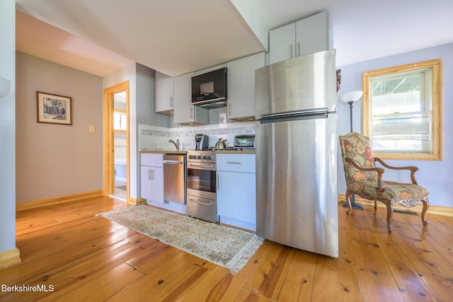 kitchen featuring backsplash, white cabinets, light hardwood / wood-style floors, and appliances with stainless steel finishes