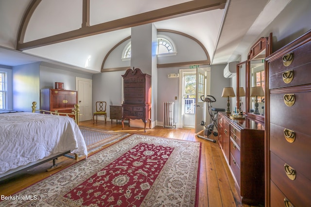 bedroom featuring a wall mounted air conditioner, light hardwood / wood-style floors, radiator heating unit, and high vaulted ceiling