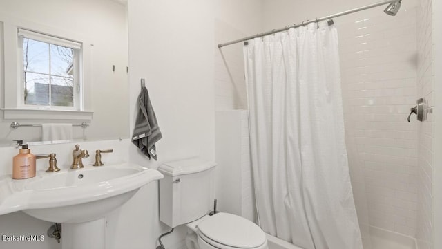 bathroom featuring toilet, tiled shower, and a sink