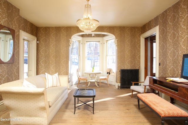 living area featuring radiator heating unit, a notable chandelier, and light wood-type flooring