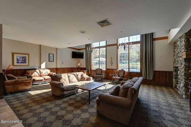 living room featuring a wainscoted wall, a stone fireplace, visible vents, and wooden walls