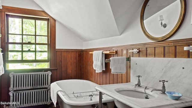 bathroom with radiator, vaulted ceiling, sink, a tub, and wood walls