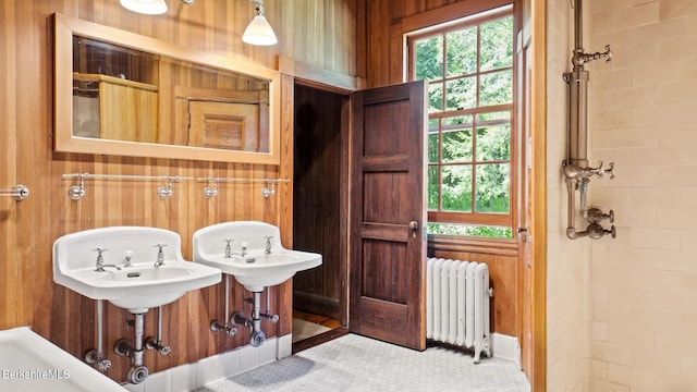 bathroom featuring wood walls, dual sinks, and radiator