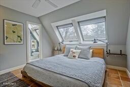 bedroom featuring baseboards, lofted ceiling with skylight, multiple windows, and ceiling fan