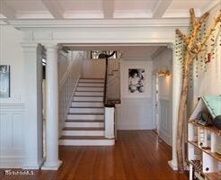 stairs featuring a decorative wall, beam ceiling, wood finished floors, ornamental molding, and coffered ceiling