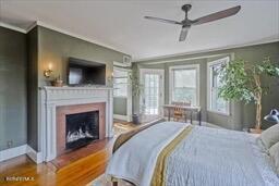 bedroom featuring crown molding, baseboards, wood finished floors, and a fireplace