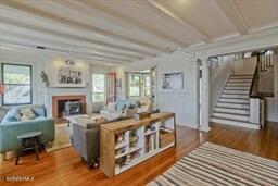 living area with stairs, wood finished floors, a fireplace, and beamed ceiling