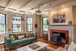living room with a wood stove, wood finished floors, a healthy amount of sunlight, and beamed ceiling