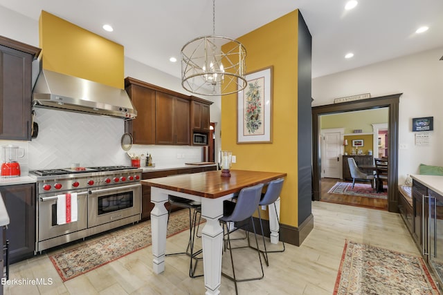kitchen with wall chimney range hood, appliances with stainless steel finishes, tasteful backsplash, a chandelier, and light wood-style floors