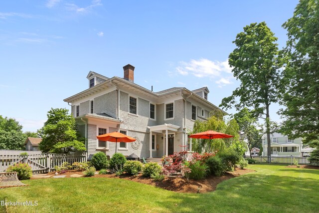 back of house featuring a lawn, fence, and a chimney
