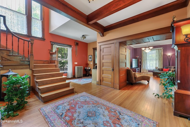 entrance foyer featuring stairway, wood-type flooring, beamed ceiling, a notable chandelier, and radiator