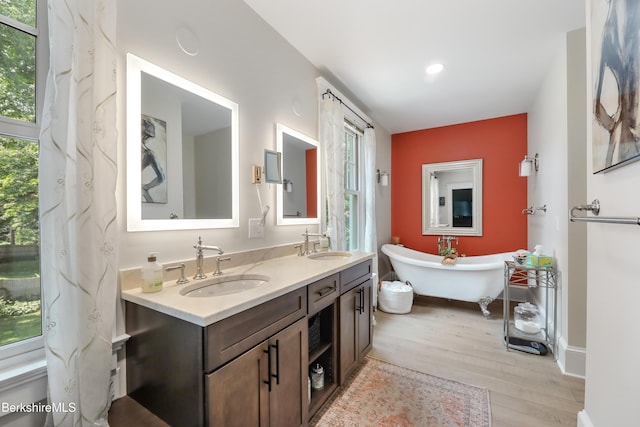 full bathroom with double vanity, a soaking tub, a sink, and wood finished floors