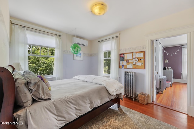 bedroom with radiator, an AC wall unit, and wood finished floors