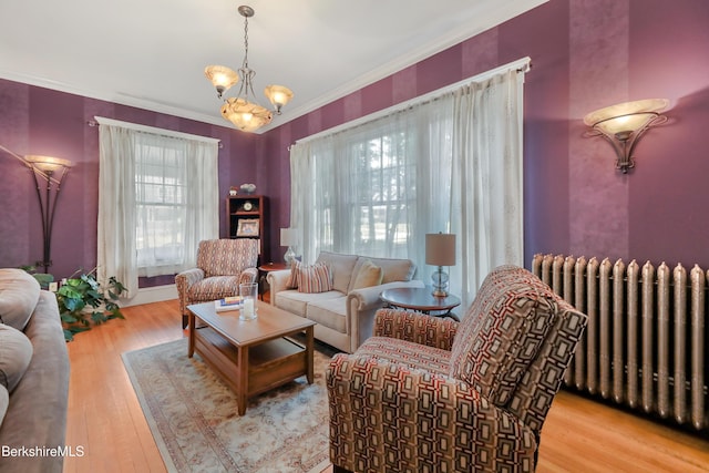 living area with wood finished floors, ornamental molding, radiator heating unit, and a notable chandelier