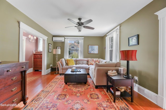 living area with a ceiling fan, baseboards, wood finished floors, and a wall mounted air conditioner