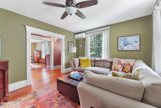 living area with ceiling fan with notable chandelier, baseboards, an AC wall unit, and wood finished floors