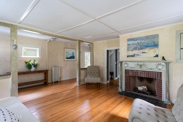 living area with radiator heating unit, wood-type flooring, plenty of natural light, and a brick fireplace