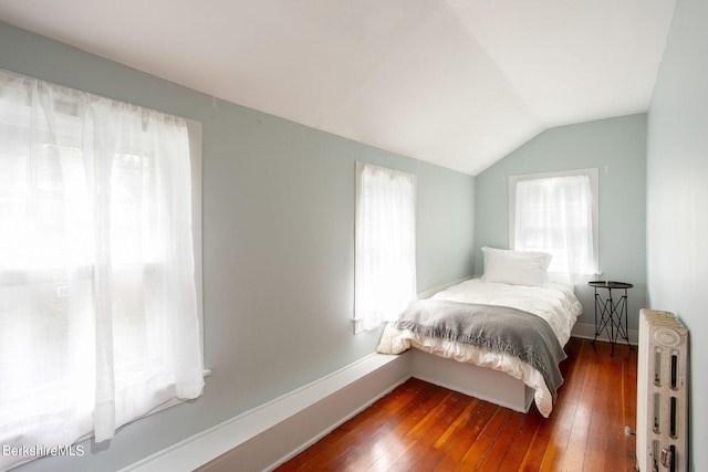 bedroom with radiator heating unit, lofted ceiling, and hardwood / wood-style flooring