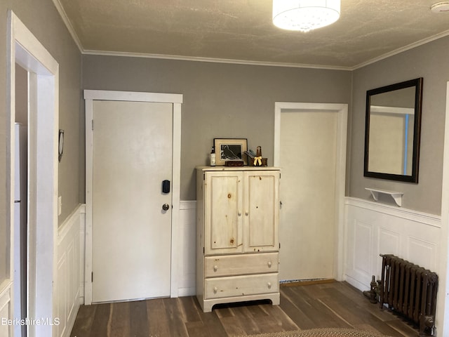 entrance foyer featuring radiator heating unit, dark wood-style flooring, wainscoting, crown molding, and a decorative wall