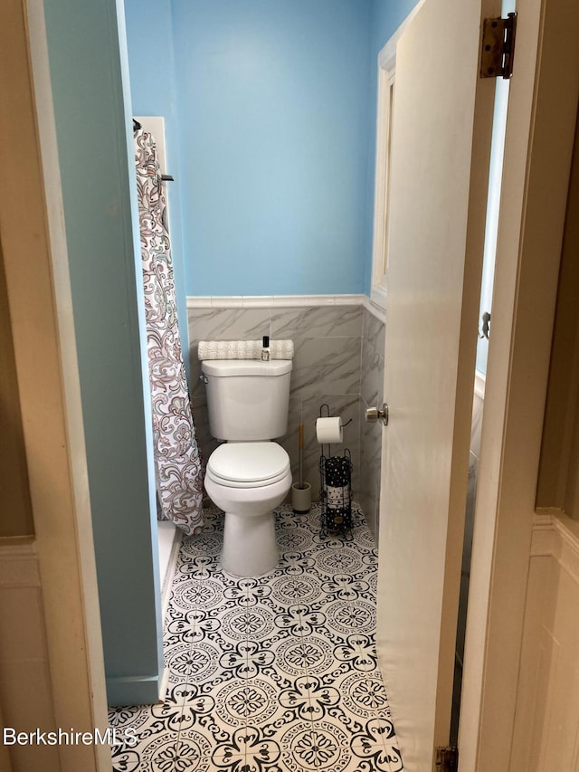 full bath with toilet, wainscoting, tile patterned flooring, and a shower with curtain
