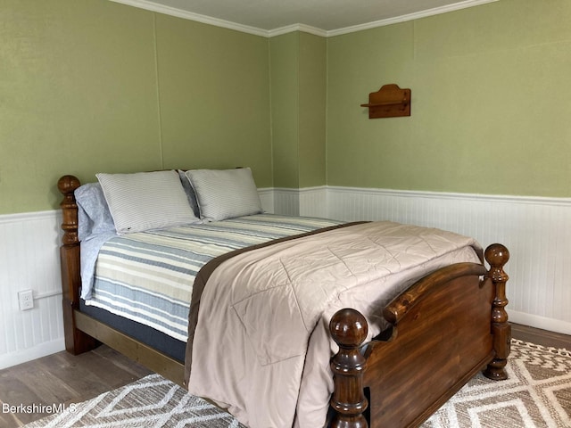 bedroom featuring wood finished floors, wainscoting, crown molding, and baseboards