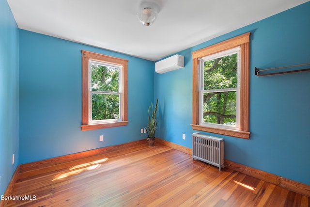 empty room with a wall mounted air conditioner, light hardwood / wood-style floors, and radiator heating unit