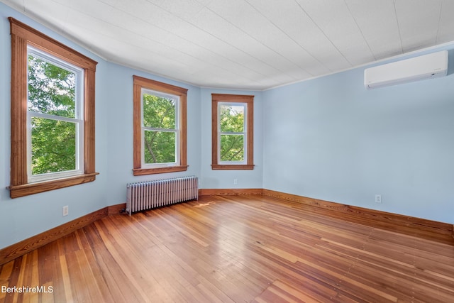 spare room with a wall mounted air conditioner, radiator heating unit, and hardwood / wood-style flooring