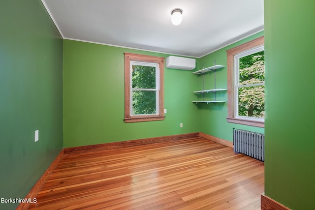 unfurnished room featuring a wall mounted air conditioner, plenty of natural light, radiator, and light hardwood / wood-style flooring