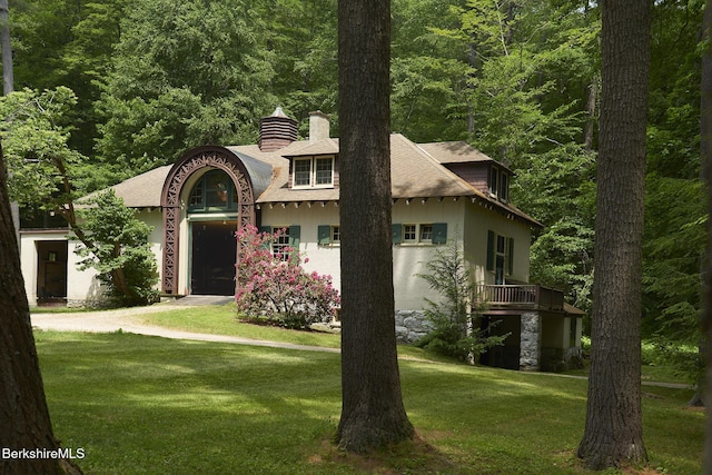 319 Under Mountain Rd, Lenox, MA 01240 - view of front of house with a chimney, a front yard, a shingled roof, stucco siding, and a forest view