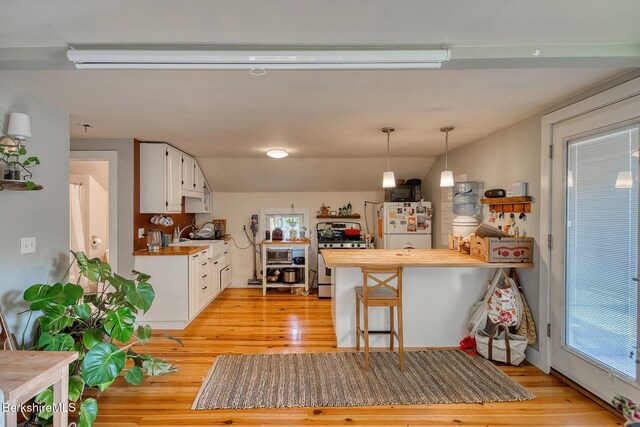 kitchen featuring stainless steel gas range oven, white refrigerator, hanging light fixtures, white cabinetry, and a breakfast bar area