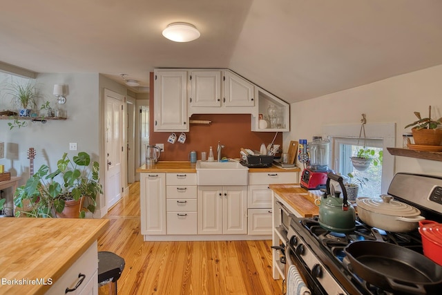 kitchen with butcher block countertops, white cabinets, sink, and stainless steel stove