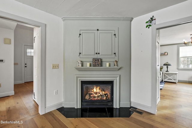 details featuring visible vents, a fireplace with flush hearth, wood finished floors, a chandelier, and baseboards